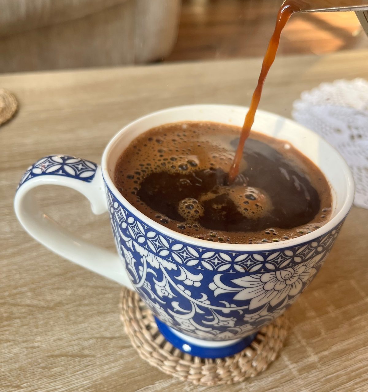 Coffee being poured into a blue and white floral porcelain cup, foam swirling on the surface