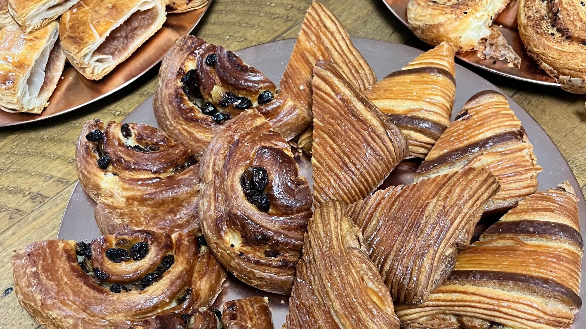 Close-up of laminated pastries and raisin swirls on a copper tray, layers glistening with glaze